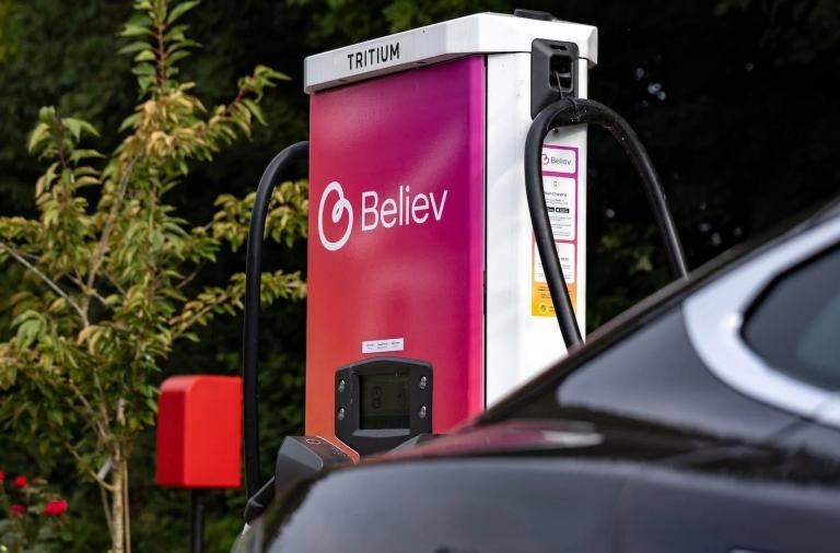 A roadside charger for electric vehicles with a pink and orange facade and the Believ logo on the side