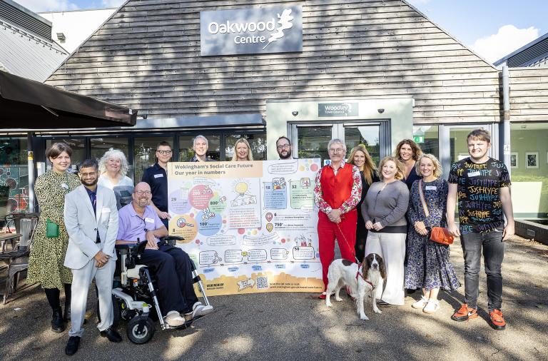 A group of people and a dog pose in front of the Oakwood centre with a sign