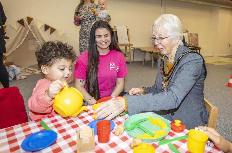 Borough Mayor Cllr Carol Jewell sits with a child who pours pretend tea