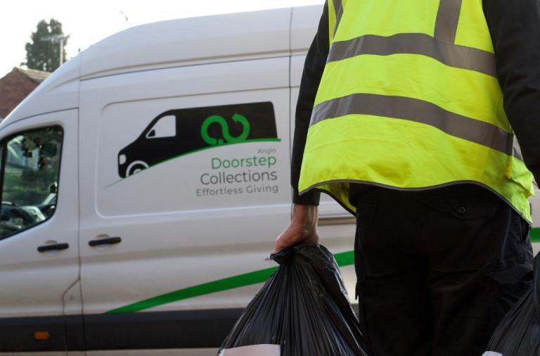 Driver carrying logo-labeled donation bags toward "Doorstep Collections" van.