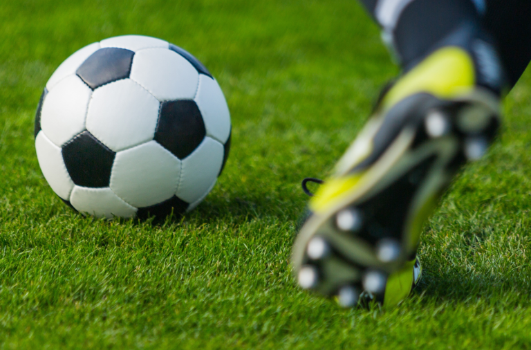 close up of a booted foot about to kick a football on a pitch