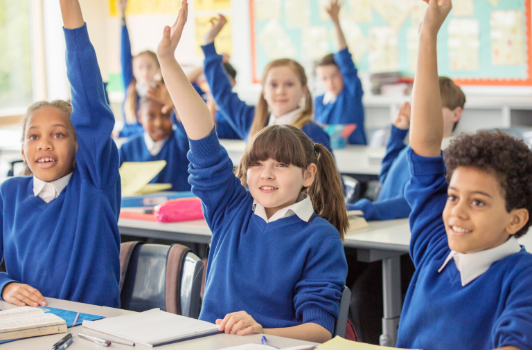 School children in class with their hands raised