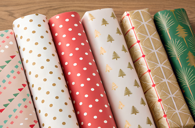 Rolls of colourful & patterned Christmas gift wrapping paper on wood.