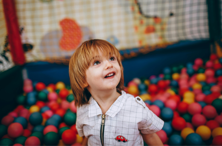 A young boy smiling in a colourful ball pit at a soft play centre