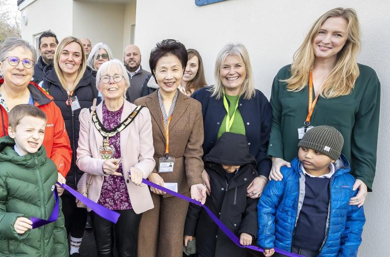 Borough Mayor Cllr Carol Jewell cuts the ribbon with Cllr Prue Bray and headteacher Li-Juan Ellerton. School children and teachers and staff are present.