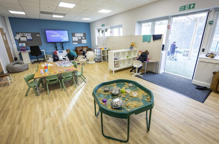 One of the classrooms with a tuff tray full of sensory items, screen, tables and chairs