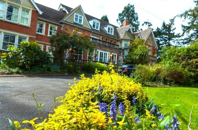 Bluebell House residential home in Wokingham, red brick building with a flower bed with yellow leaves and purple flowers in the foreground