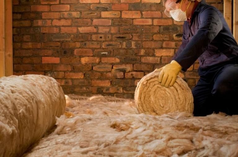 Worker laying rolls of loft insulation in an attic.