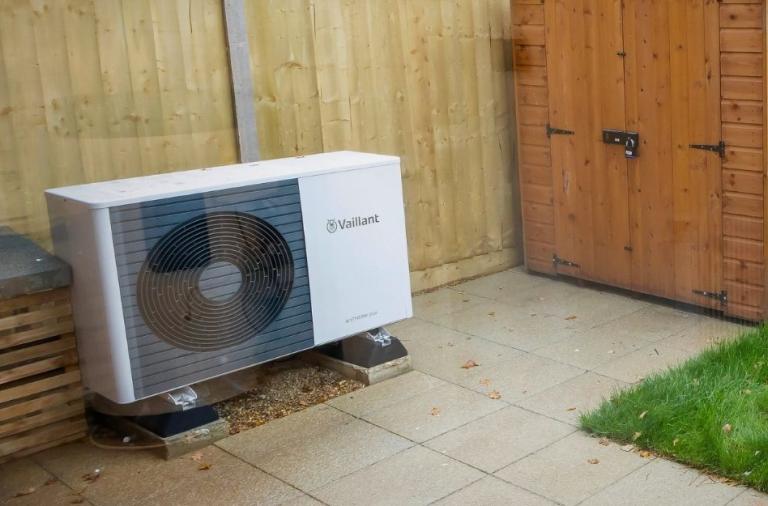 Outdoor heat pump unit installed beside a wooden fence and shed.