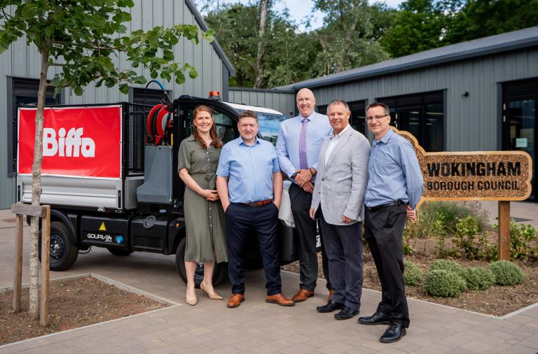 Group of representatives standing beside a waste collection vehicle and Wokingham Borough Council sign to mark the first month of the council's new waste collection and street cleansing contract with Biffa.