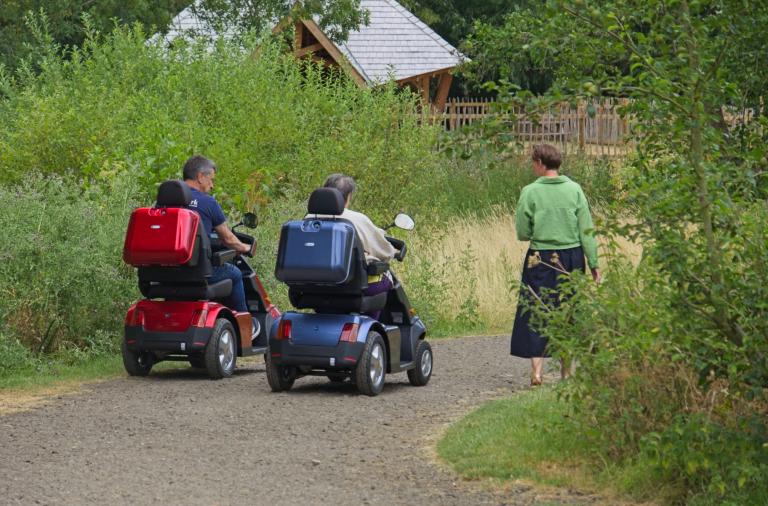 Two mobility scooter users travel along a path through Dinton Pastures Country Park.