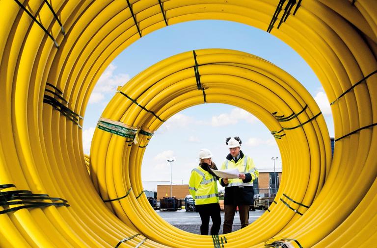 Two SGN engineers in green hi vis, viewed through a coil of yellow plastic gas pipes
