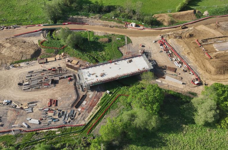 A new bridge is laid over a river as part of a road which is still half built and mostly a dirt track