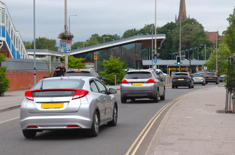 A line of cars drives past Wokingham station, with the multi-storey car park in the background