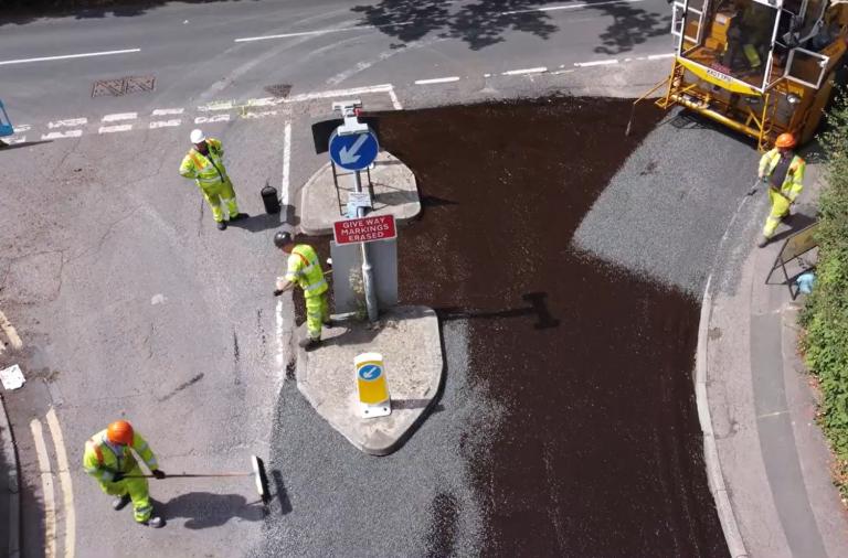 Aerial view of council crews dressing a road surface, with a vehicle laying chippings and crews sweeping up behind