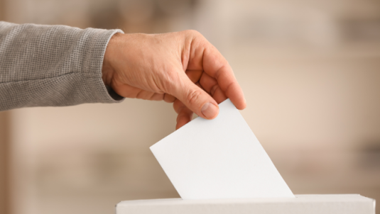 A hand over a ballot box, posting a ball