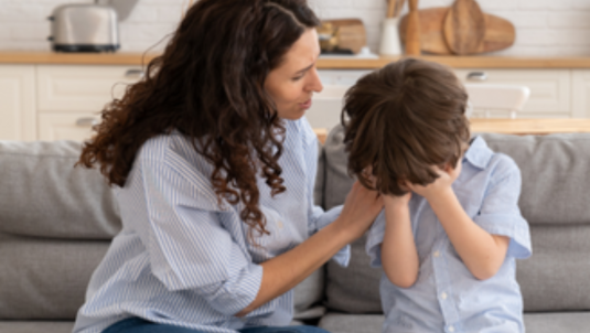 A woman comforts an unhappy child while sat on the sofa