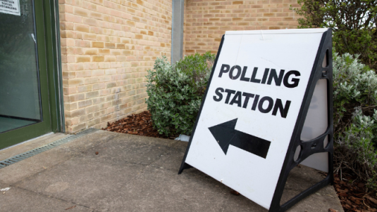An A-board sign outside a polling station which says 'polling station' and points towards the entrance