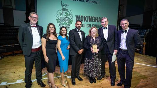 Photo of seven men and women in formal evening wear accepting an award, in front on a screen with Wokingham Borough Council's logo on it