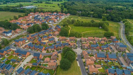 An aerial view of an area where new housing is being built, with large areas of green space and trees as well as parks with footpaths