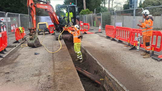 Workers in high viz digging up a section of the road where utliity pipes are underneath