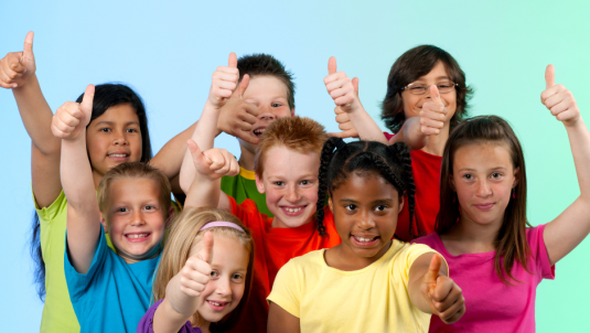 A group of eight children wearing brightly coloured tshirts smiling at the camera and giving a thumbs up