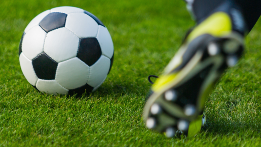 close up of a booted foot about to kick a football on a pitch