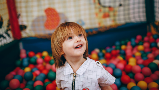 A young boy smiling in a colourful ball pit at a soft play centre