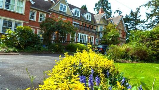 Bluebell House residential home in Wokingham, red brick building with a flower bed with yellow leaves and purple flowers in the foreground
