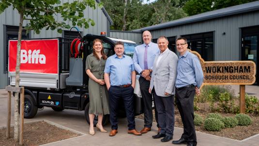 Group of representatives standing beside a waste collection vehicle and Wokingham Borough Council sign to mark the first month of the council's new waste collection and street cleansing contract with Biffa.
