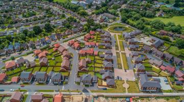 An aerial view of an area where new housing is being built, with large areas of green space and trees as well as parks with footpaths