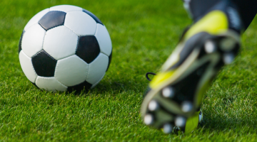 close up of a booted foot about to kick a football on a pitch