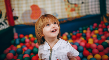 A young boy smiling in a colourful ball pit at a soft play centre