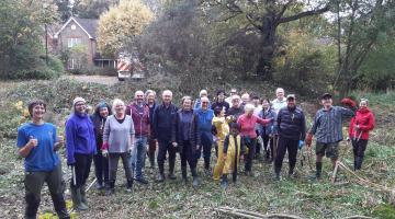 A large volunteer group standing on cleared woodland, posing together after conservation work.