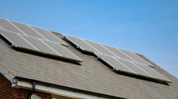 Solar panels fitted on a roof under a clear blue sky.
