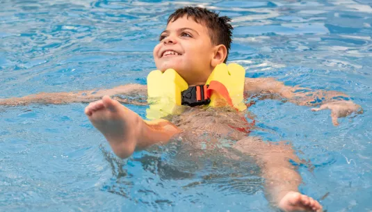 A boy smiling and floating on his back in a swimming pool