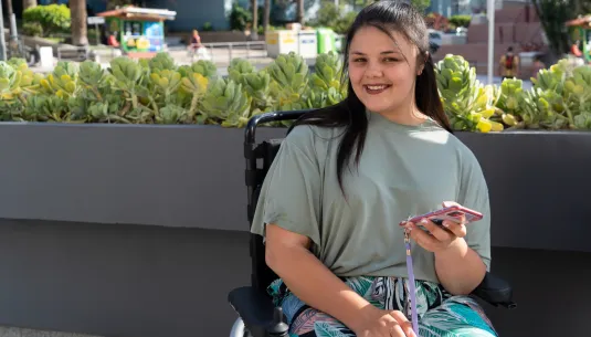 A teenage girl in a wheel chair smiling while holding her phone