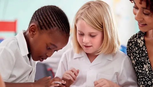 Two children in a classroom using a tablet together with their teacher