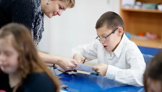 A teacher helping a child to use scissors