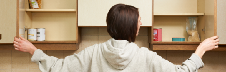 A woman opens two kitchen cupboards showing a few tinned goods left at the back of the cupbard