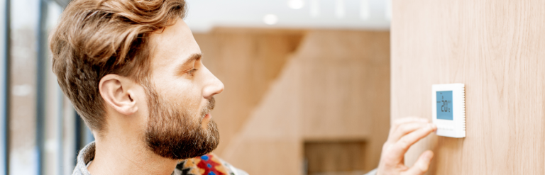 Man adjusting his heating thermostat down despite cold weather