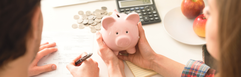 A couple looking at a piggy bank while assessing their finances