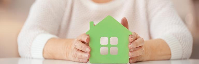 Older lady holding a green card board cut out of a housing