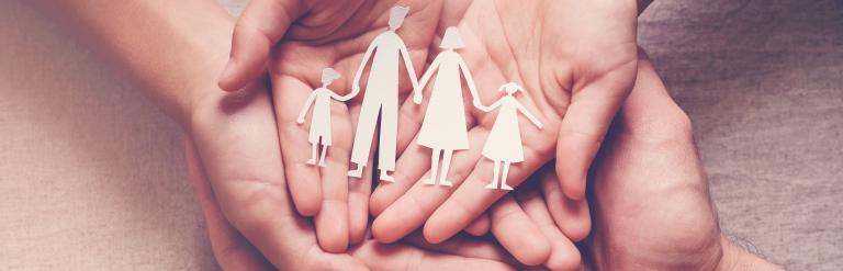 Different peoples hands, laid on top of each other facing upwards with paper cut out of a family