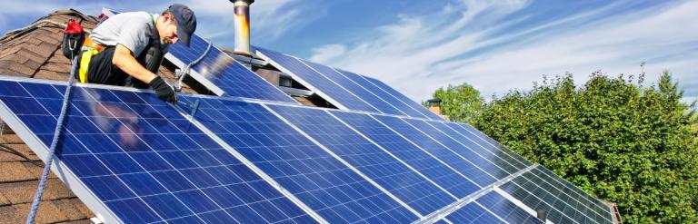 A man on a roof installing a solar panel array 