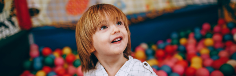 A young boy smiling in a colourful ball pit at a soft play centre